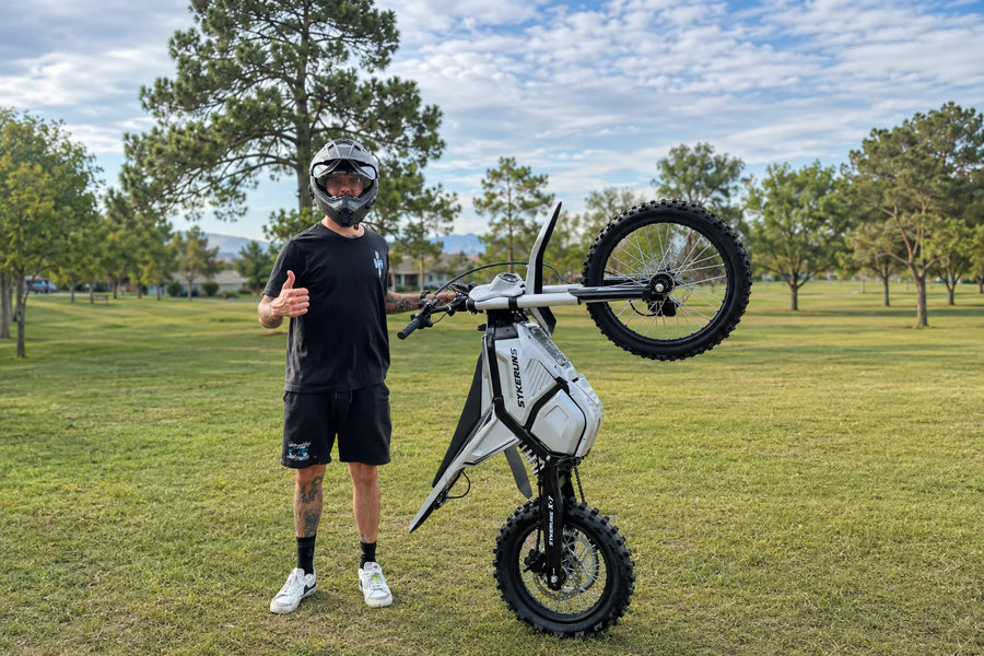 Adult rider standing with a SYKERUNS X7 electric dirt bike in an outdoor park