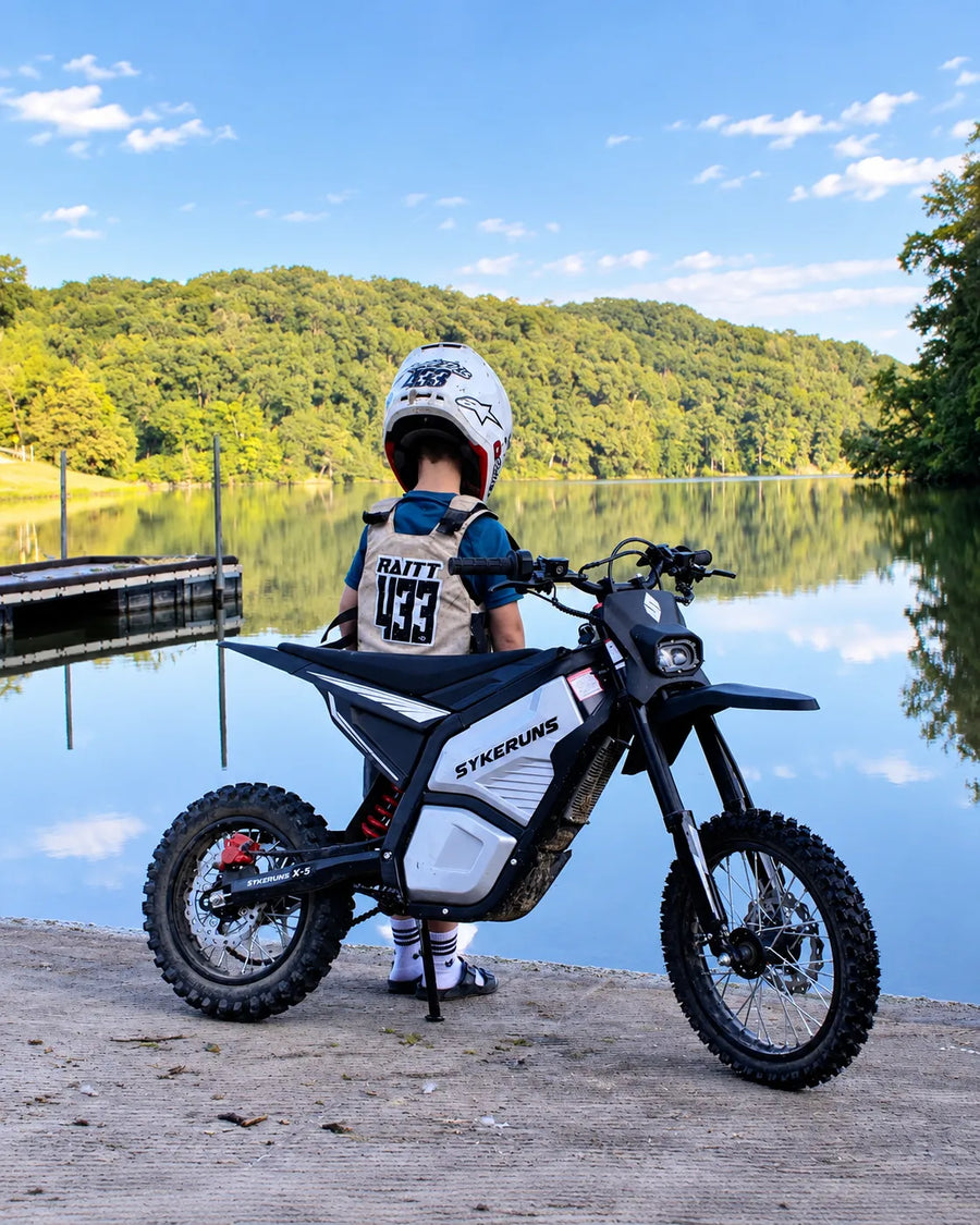 Helmeted rider with a SYKERUNS X5 electric dirt bike overlooking a lake