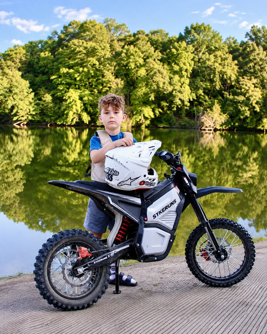 Young rider with a SYKERUNS X5 electric dirt bike beside a scenic lake
