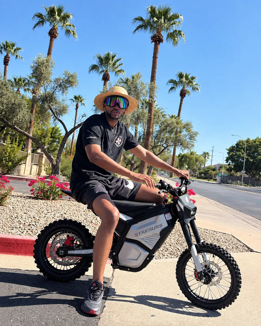Real rider on a SYKERUNS X5 electric dirt bike outdoors under palm trees