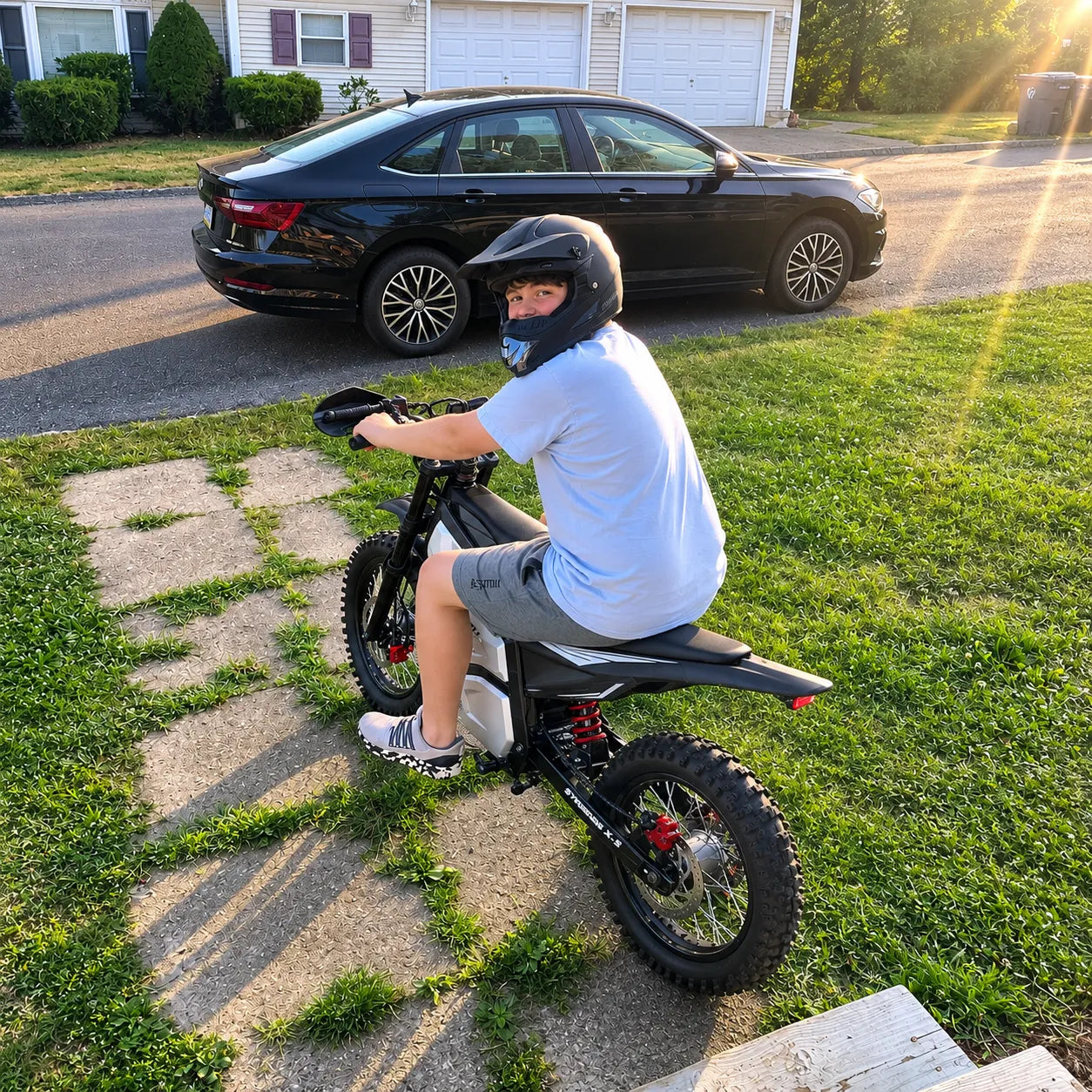 Real rider sitting on a SYKERUNS X5 electric dirt bike outside a home garage