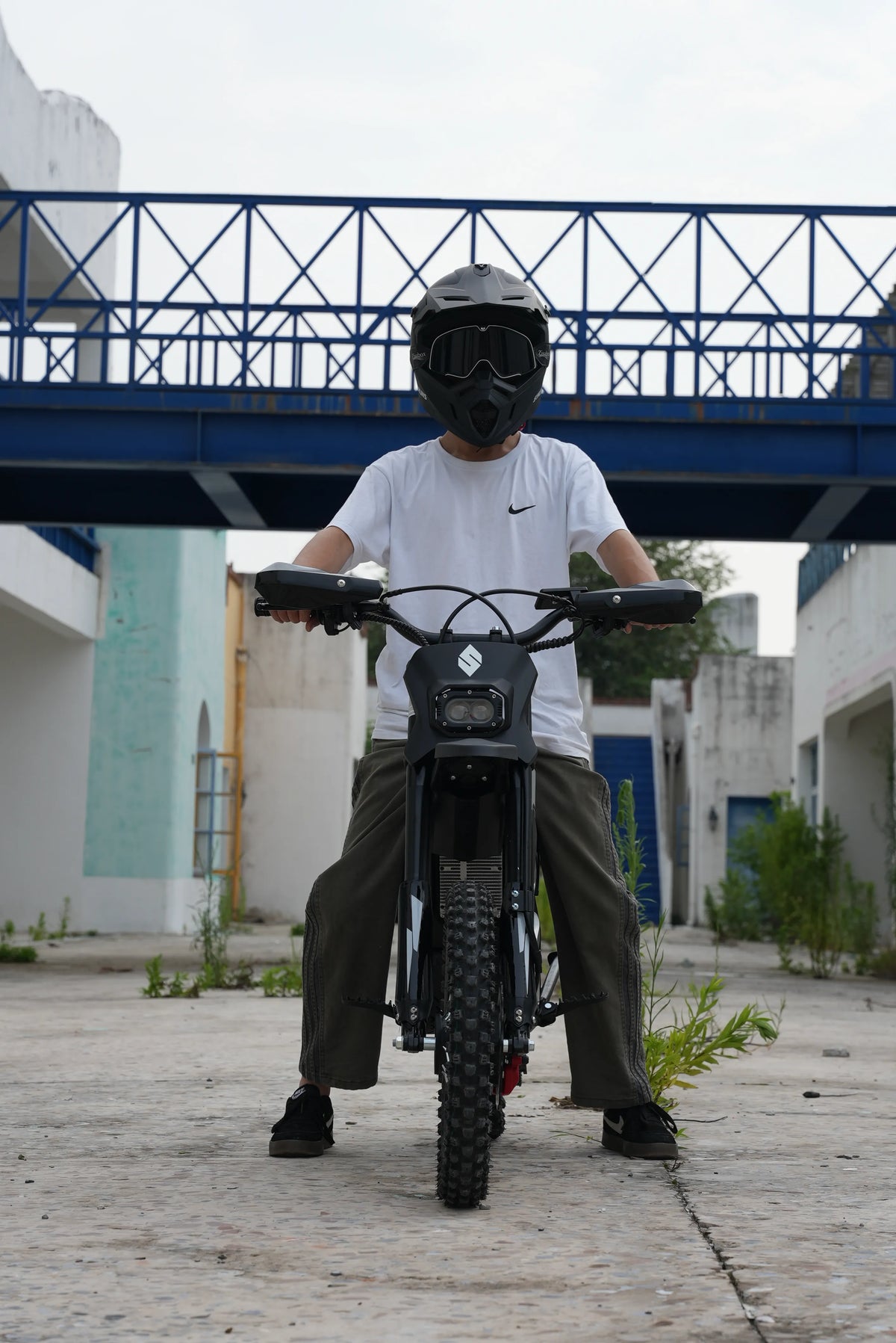 Helmeted rider on a SYKERUNS X5 electric dirt bike in an urban outdoor setting
