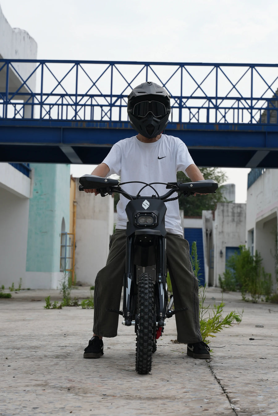 Helmeted rider on a SYKERUNS X5 electric dirt bike in an urban outdoor setting