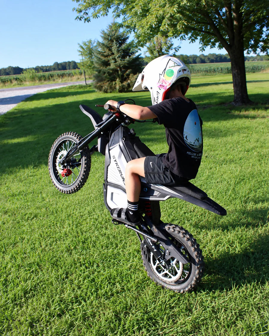 Helmeted rider performing a wheelie on a SYKERUNS X5 electric dirt bike on grass