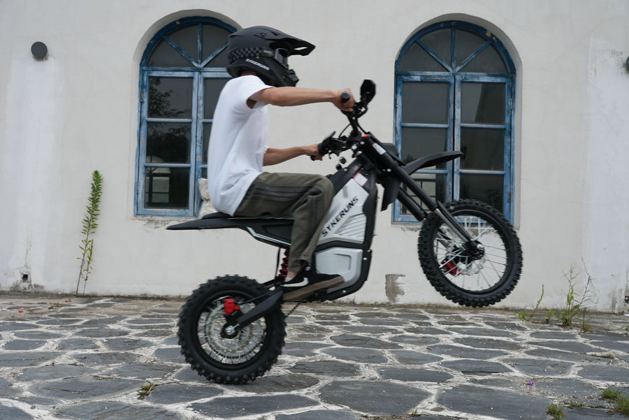 Helmeted rider performing a wheelie on a SYKERUNS X5 electric dirt bike outdoors
